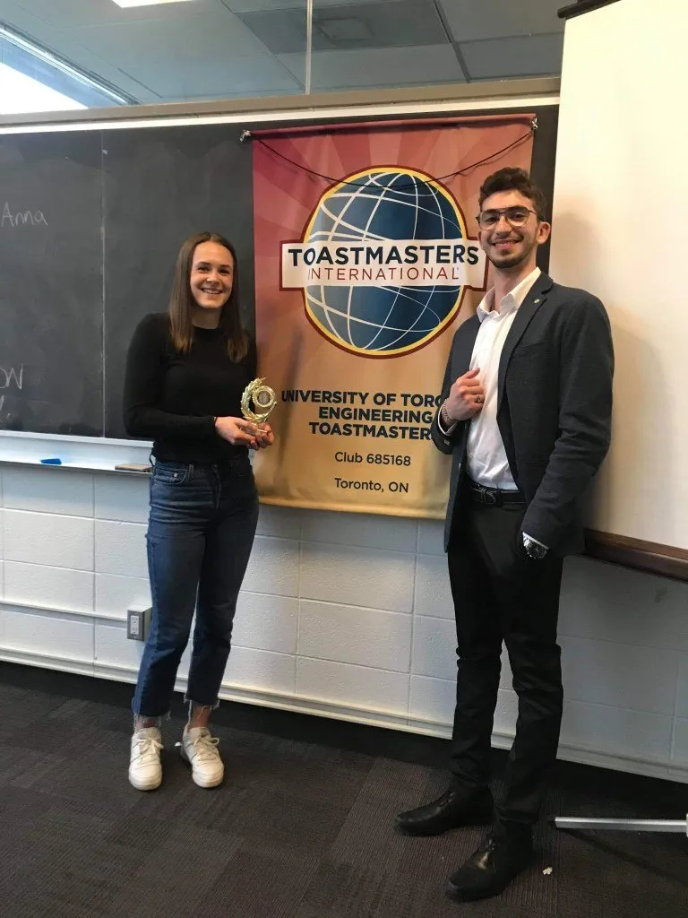 Anna Crone holding a trophy next to Youssef in front of the University of Toronto Engineering Toastmasters banner