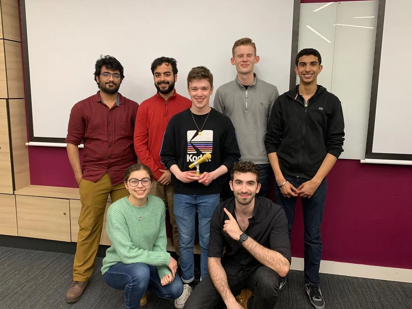 Jonah holding a golden microphone trophy with Youssef and members of the University of Birmingham Public Speaking Society