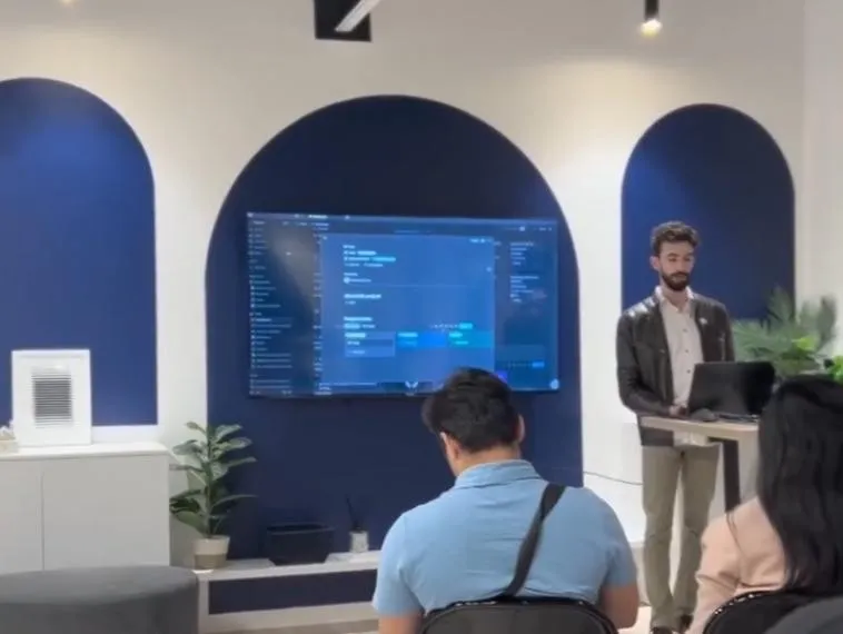 Youssef speaking at a podium beside a screen showing Notion, with the audience seated in front