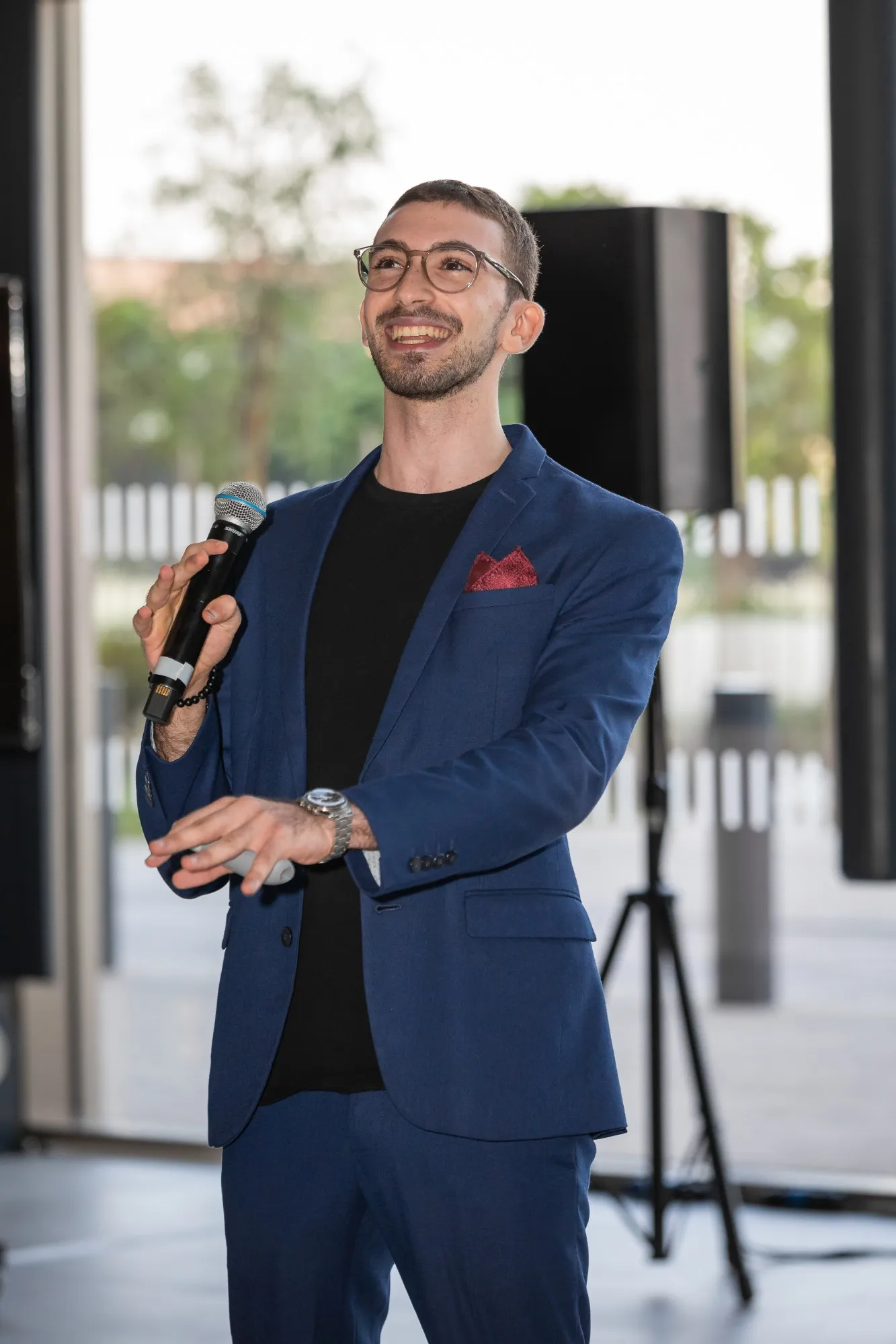 Youssef in a blue suit, smiling and holding a microphone while hosting the first annual club awards